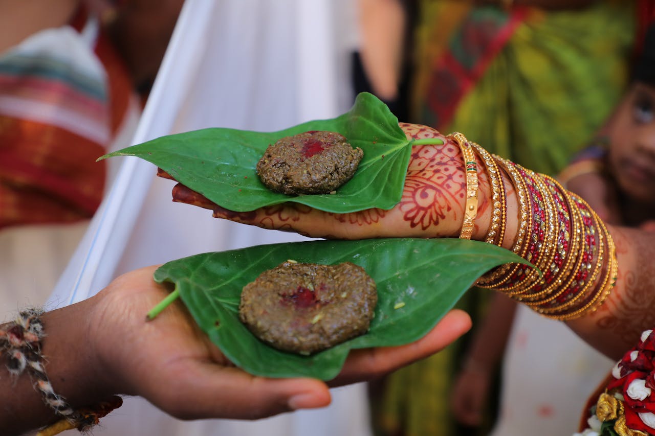 Close-up of henna-decorated hands holding traditional food on leaves